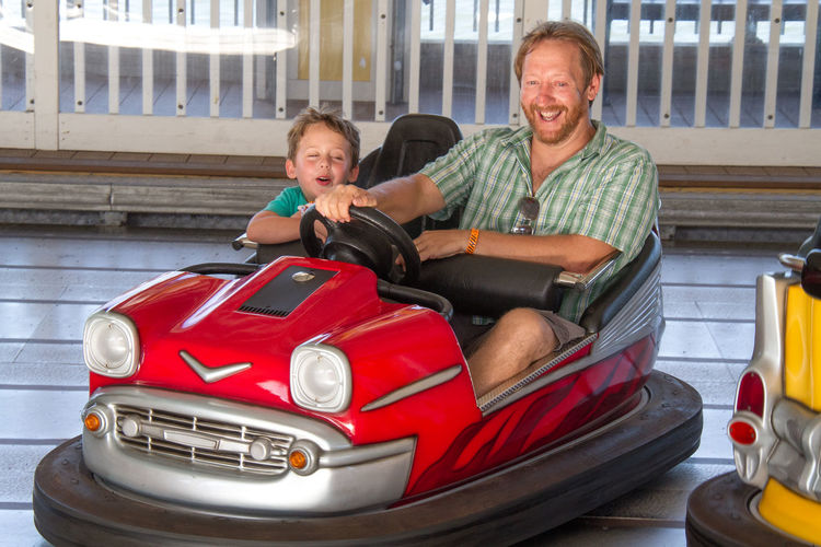 Happy father with son driving bumper car in amusement park
