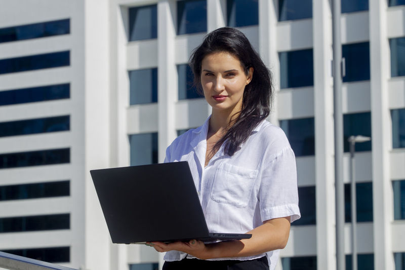 Young woman using laptop while standing against building