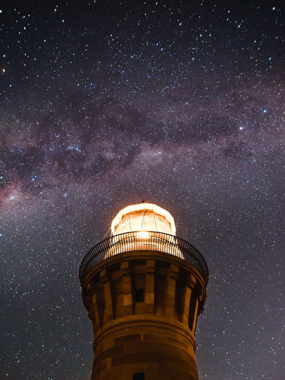 Low angle view of illuminated lighthouse against sky at night