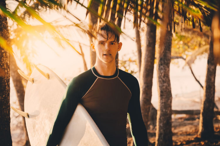 Portrait of confident young man with surfboard at beach