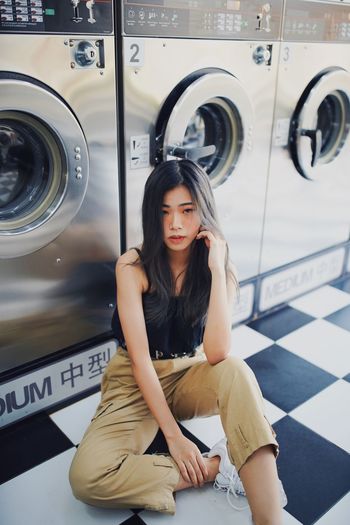 Portrait of woman sitting against washing machine