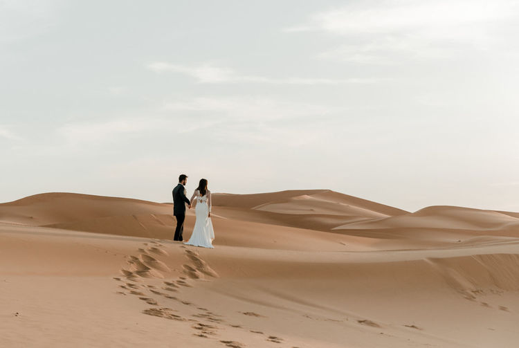 A couple in their wedding dresses walk barefoot through the desert at dawn. wedding concept