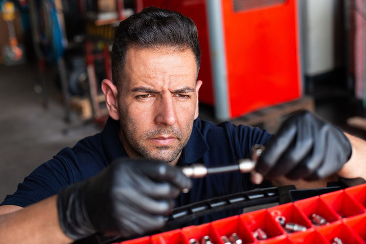 Adult man in latex gloves examining instrument over tool box during work in modern workshop