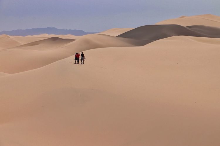 People walking on desert against clear sky