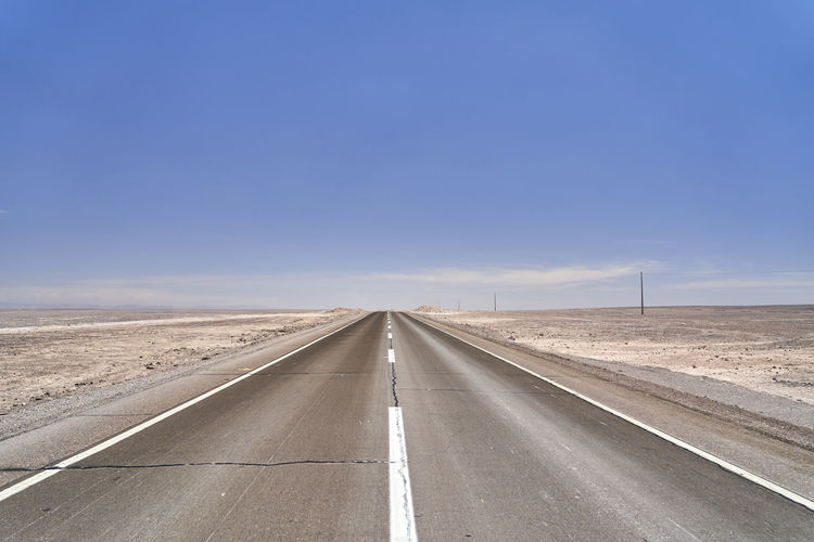 Dark, black tarmac road to nowhere leading straight to the horizon in the atacama desert of chile. 