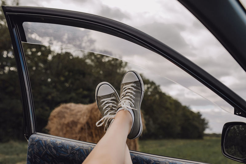 Legs in stylish sneakers, car window, autumn field with haystacks. rest stop car trip. local travel