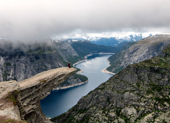Mid distance of person sitting on cliff against rivercliffdanger