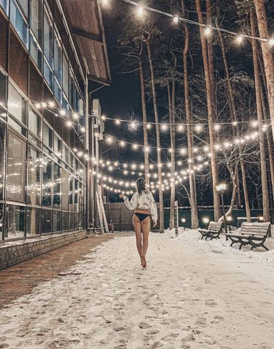 Rear view of woman in panties walking on illuminated street at night