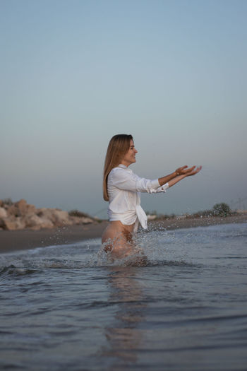 Beautiful woman sitting at beach against sky
