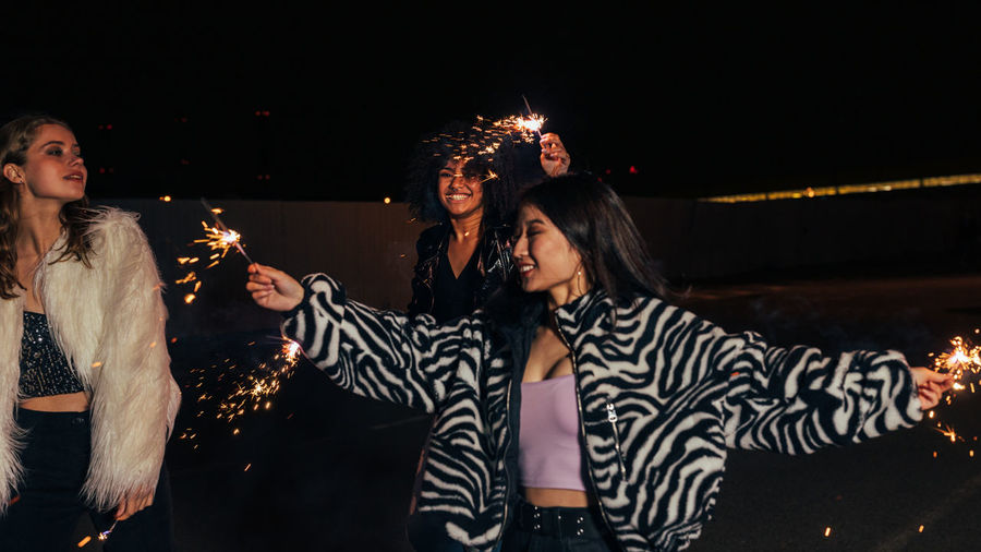 Smiling young women holding sparkler enjoying in night club