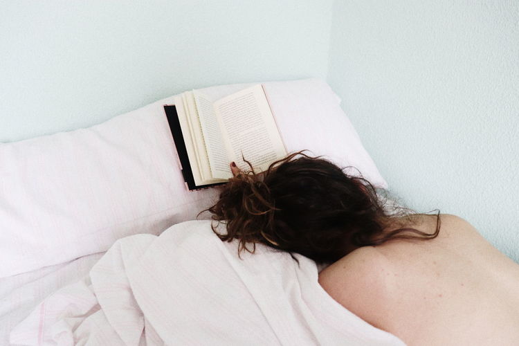 High angle view of topless teenager lying on bed by book at home