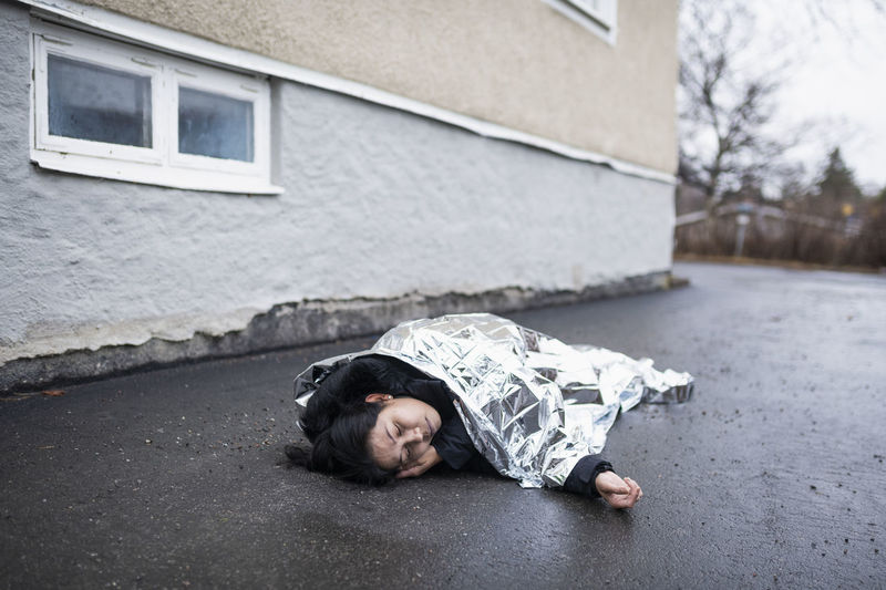 Unconscious woman in medical shock lying under emergency blanket in street