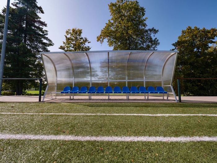 Beats on outdoor stadium players bench chairs with blue paint below transparent roof.