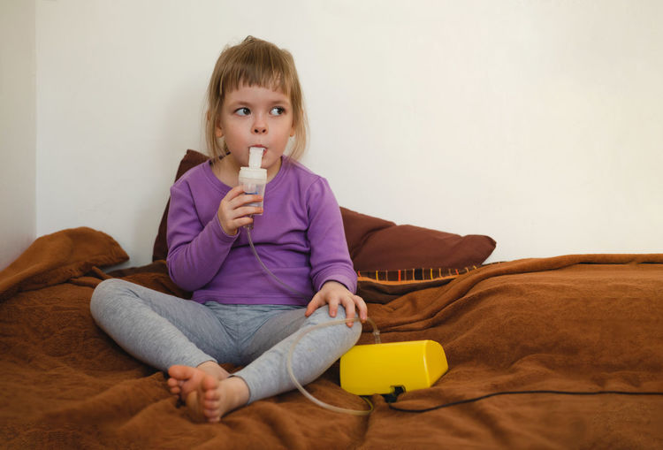 Sick child lies in bed and makes inhalation using a nebulizer. treatment of bronchitis