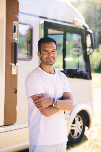 Portrait of confident mature man standing with arms crossed by travel trailer