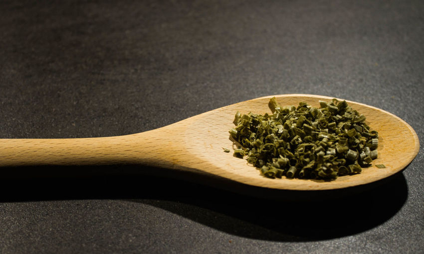 Close-up of chopped chive in wooden spoon on table