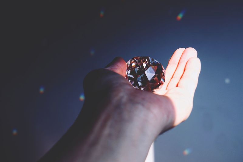 Close-up of hand holding diamond against blurred background