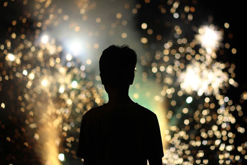 Rear view of silhouette man against illuminated sparklers at night