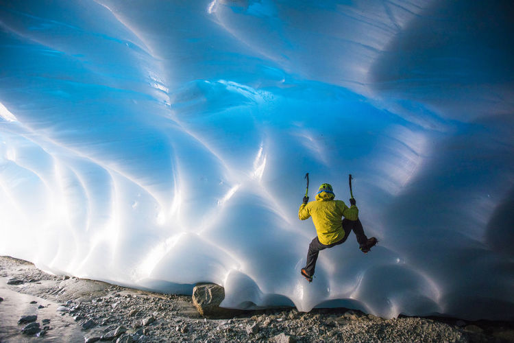 Mountaineer ice climbing on glacial ice in ice cave.