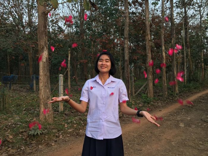 Petals falling on smiling teenage girl gesturing while standing outdoors