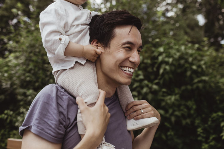 Smiling father carrying male toddler on shoulder at park