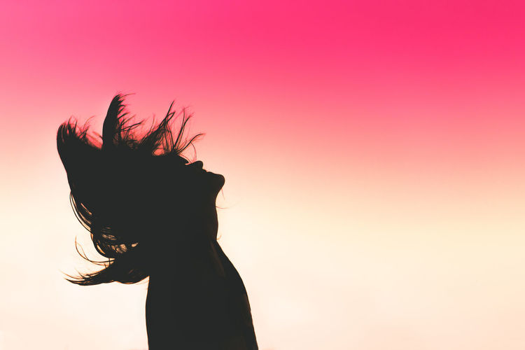 Side view of silhouette woman tossing hair against dramatic sky during sunset