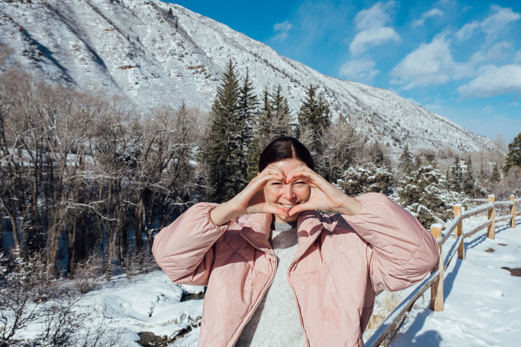Outdoor portrait of happy woman traveler in winter clothes on snowy mountains background. 