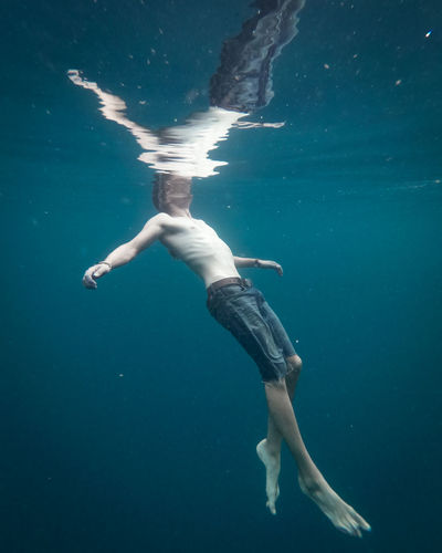 Man wearing short jeans swimming and floating in clear water