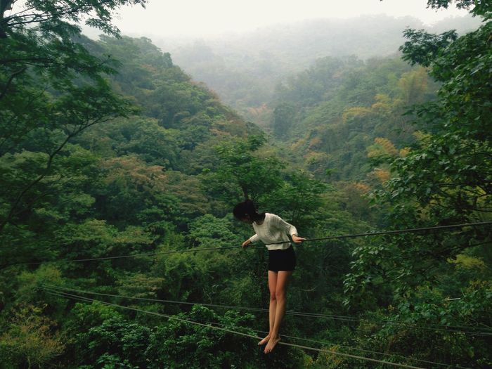 Full length of young woman standing on rope in forest