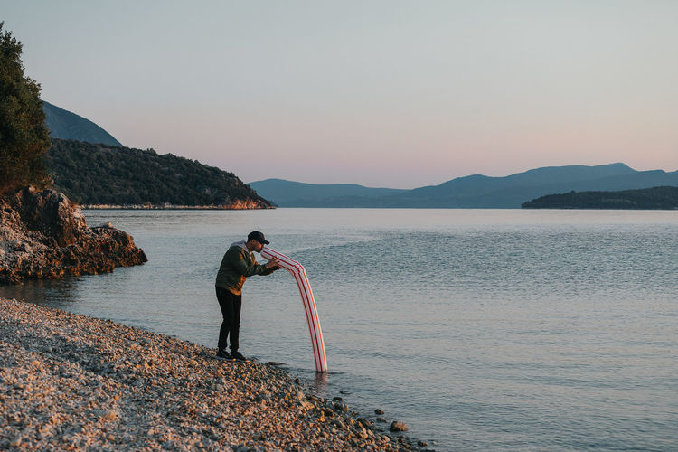 Man blowing drinking straw in sea against sky