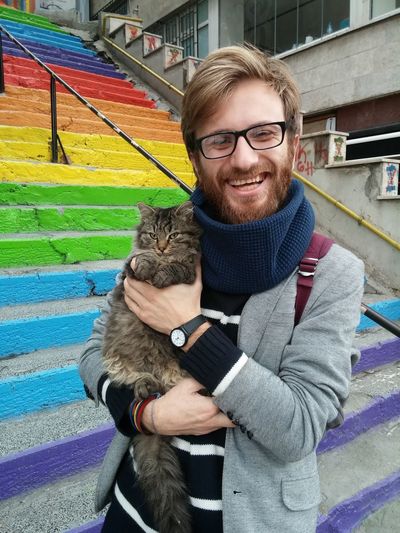 Portrait of happy man carrying cat while standing on colorful steps