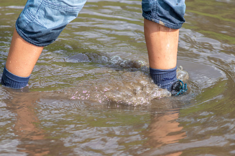 Young boy with blue shorts, wet socks and wet shoes stands in floodwater after the dike was broken