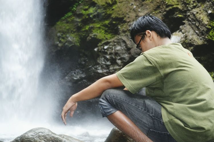 Man crouching against waterfall