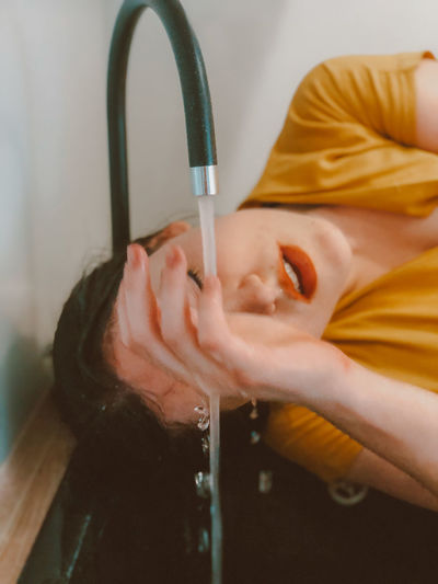 Close-up of woman by water flowing from faucet at home