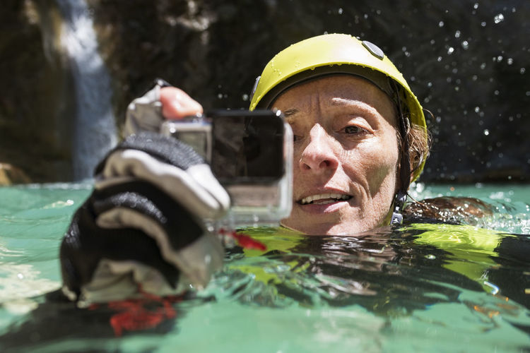 Close-up of female rock climber filming while swimming in river