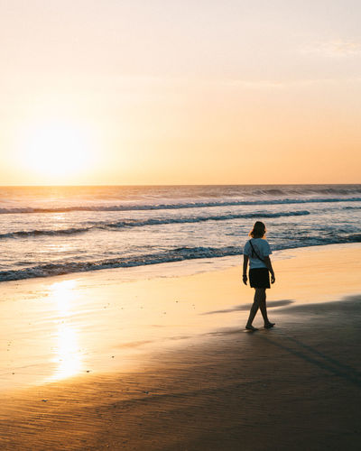 Woman walking at beach against sky during sunset