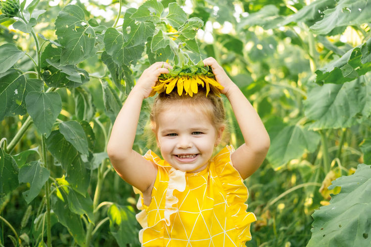 Happy little kid girl playing in blooming sunflower field on sunny summer day