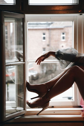 Low section of woman sitting on window sill at home