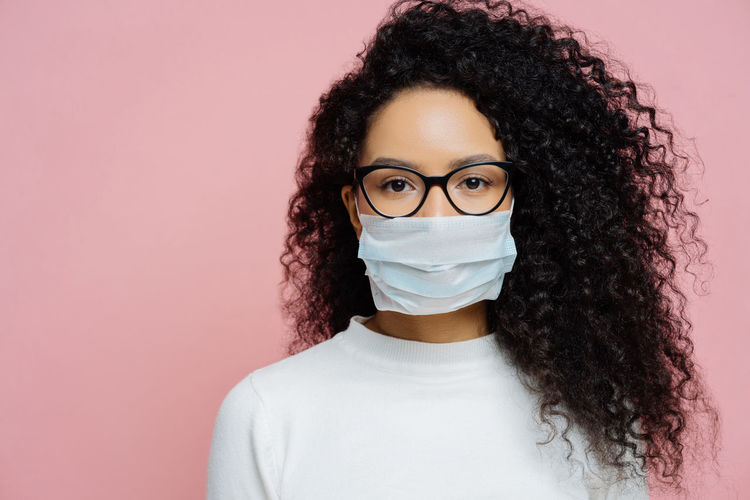 Woman with curly hair wearing mask against colored background