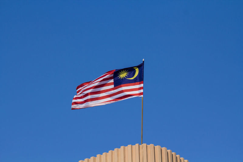 Low angle view of malaysian flag against clear blue sky