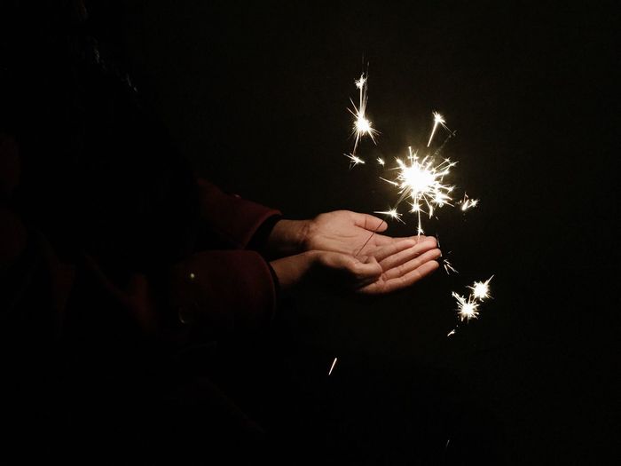 Cropped hands of man holding lit sparkler at night