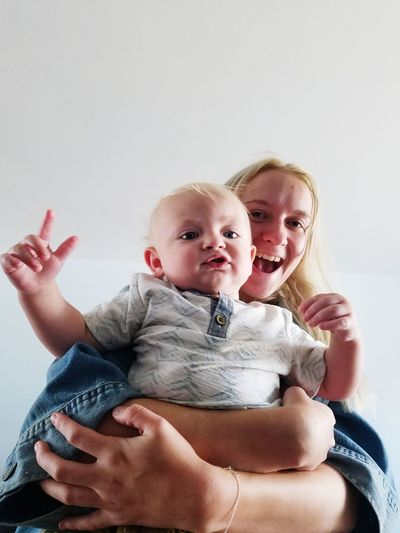 Low angle portrait of cheerful mother holding son against ceiling