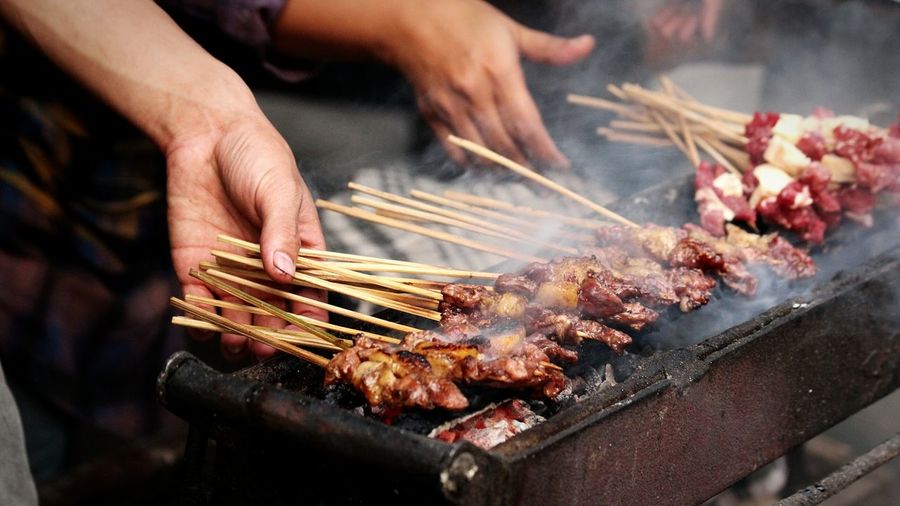 Cropped image of people with satay on barbecue grill at market stall