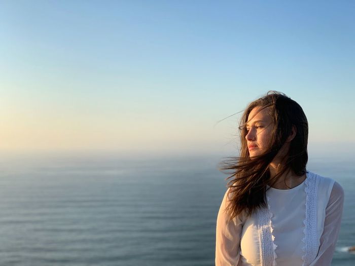 Beautiful woman standing by sea against clear sky
