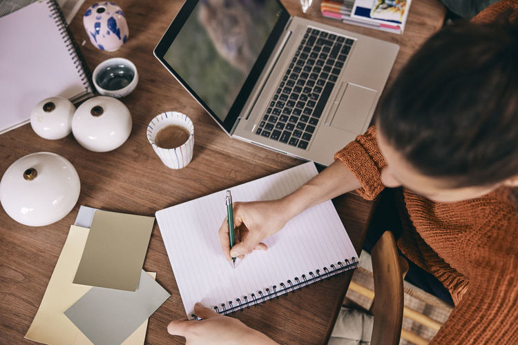 High angle view of female freelancer preparing to-do list in spiral book while sitting with laptop at home