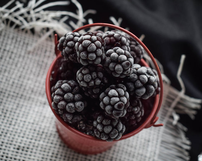 Frozen blueberries in a red bucket on the table in summer 2018