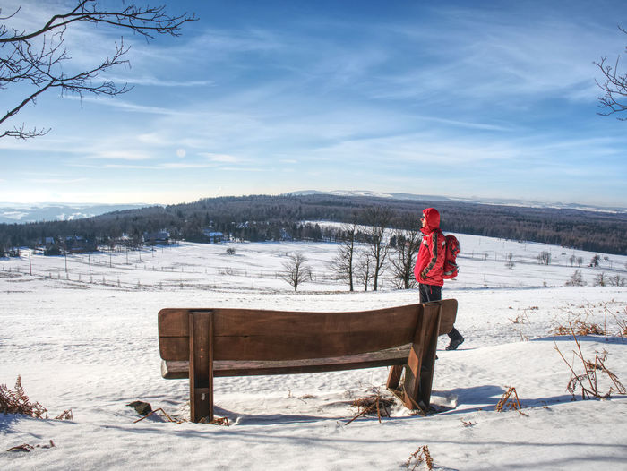 Man tourist is resting at wooden bench in winter landscape. hiker with red backpack