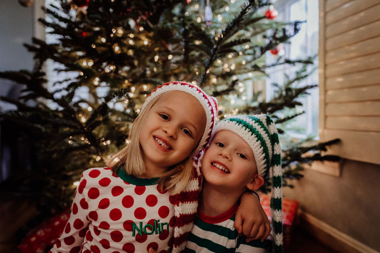 Portrait of siblings in costume sitting against christmas tree at home