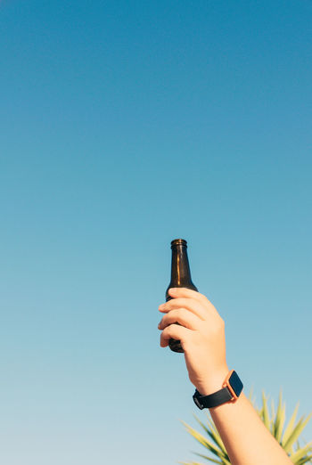 Low angle view of hand holding bottle against blue sky