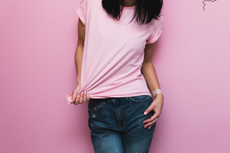Midsection of woman standing against pink wall